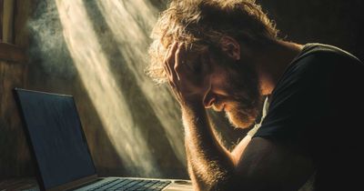 Man sitting at laptop with head in hands and sunlight streaming down on him