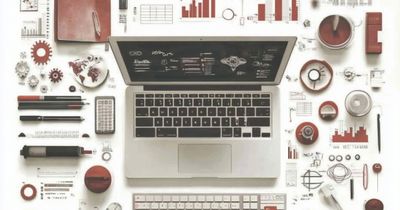 Top down view of a Laptop surrounded by cups pens graphs charts and other paraphernalia.