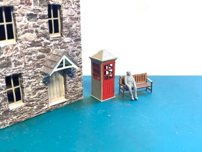 Model cottages with old phone box and man sitting on bench.