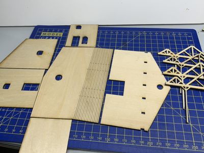 Third building - laser cut parts from 2mm basswood laid out on a blue cutting mat.